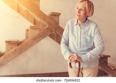 Pleasant thoughtful aged woman standing with a walking stick - Powered by Shutterstock