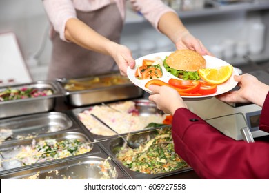 Pleasant woman giving lunch to school girl in cafeteria - Shutterstock ID 605927558