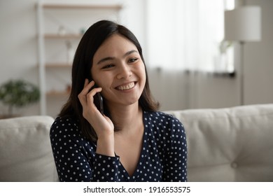 Pleasant young asian woman sit on sofa speak on smartphone holding device at ear listen to positive news. Happy millennial female enjoy chat by cell with good friend smiling relaxing having nice talk - Shutterstock ID 1916553575
