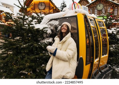 Pleasant young caucasian woman smiling with closed eyes stands in city centre in Chritmas time. Brunette wears casual winter clothes. Winter holidays concept.