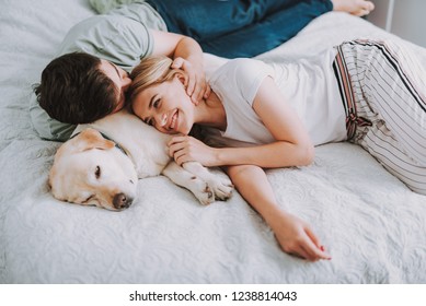 Pleasant young couple having rest in bed while their dog sleeping nearby - Powered by Shutterstock