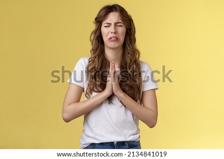 Please beg you. Sobbing timid insecure distressed cute whining girl crying upset close eyes grimacing hold hands pray pleading asking favour apologizing sincere hope for pity yellow background