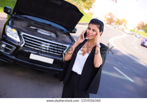 Please come as fast as you can! Beautiful young\
woman talking on mobile phone and looking frustrated  while\
standing near car\
outdoors