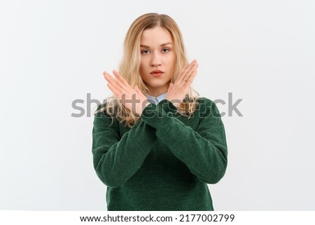 Please, do not, stop. Young serious woman with fair-haired in casual clothes, crossing arms and palms doing negative sign, prohibit, forbid something bad. Indoor studio shot on white background