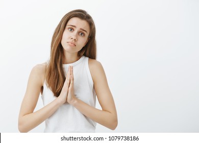 Please, forgive me darling. Portrait of timid cute caucasian female coworker in casual outfit, holding hands in pray, lifting eyebrows and tilting head while asking apology or favor, begging for help
