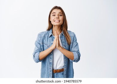 Please help me. Cute girl need something, begging for favour with needy face, holding hands in pleading pose, standing against white background