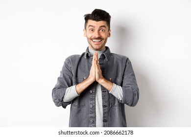 Please help me. Smiling cute man holding hands in namaste gesture, asking for favour, saying thank you, looking hopeful and excited at camera, standing on white background