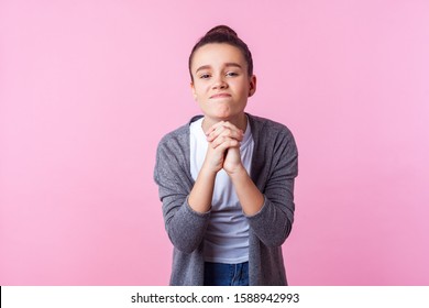 Please Let Me Do This! Portrait Of Brunette Teen Girl With Bun Hairstyle In Casual Clothes Holding Hands In Prayer, Looking With Imploring Expression, Begging Permission. Studio Shot, Pink Background