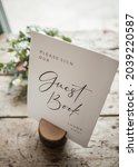 Please sign our guestbook sign at wedding celebration held standing up in wooden stand.  Flowers behind the message card  and rustic old wood table with natural light.