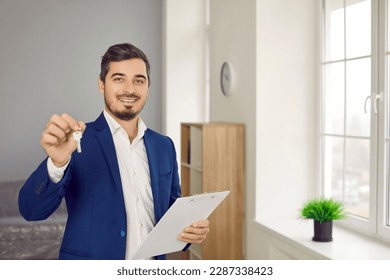 Please take your keys. Portrait of smiling young realtor or property owner who offers to get key to new apartment or house. Handsome caucasian man in suit holds key and clipboard and looks at camera. - Powered by Shutterstock