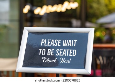 Please wait to be seated sign standing at the front of a restaurant. Sidewalk cafe hostess stand with message signboard for clients - Shutterstock ID 2200378823