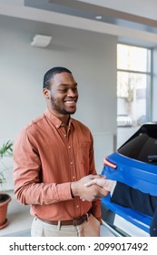 Pleased African American Man Shaking Hands With Car Dealer Near Blurred Auto