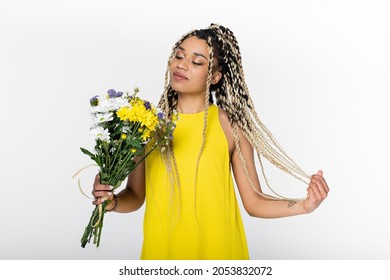 pleased african american woman touching dreadlocks while looking at colorful flowers isolated on white