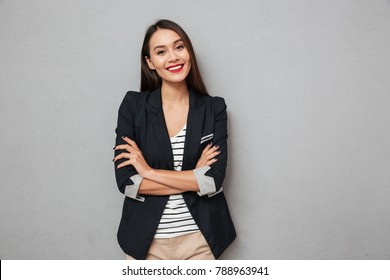 Pleased asian business woman and crossed arms looking at the camera over gray background