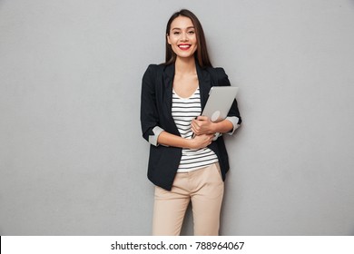 Pleased Asian Business Woman Holding Laptop Computer And Looking At The Camera Over Gray Background