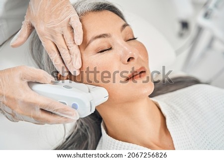 Pleased Asian patient enjoying the procedure of smoothing skin