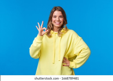 Pleased Blond Girl Left Satisfied With Trying Product Or Company Service, Smiling Delighted And Show Okay, Good Gesture, Rate Excellent Movie, Make No Problem Or All Fine Gesture, Blue Background