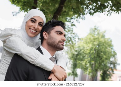 pleased bride in hijab hugging muslim groom in suit