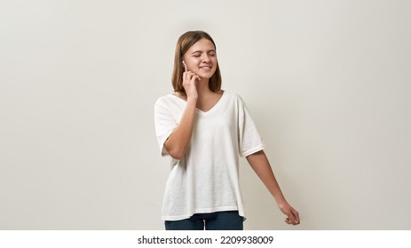 Pleased Caucasian Teenage Girl With Closed Eyes Push On Wireless Earphone For Choose Music. Blonde Female Of Zoomer Generation. Modern Youngster Lifestyle. White Background. Studio Shoot. Copy Space