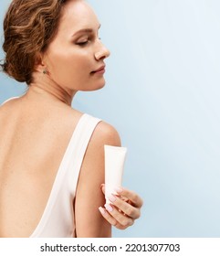 Pleased caucasian woman holding near her shoulder template cosmetics tube of sunscreen cream enjoying daily skincare treatment routine, showing mockup cosmetic package, studio portrait, rear view. - Shutterstock ID 2201307703