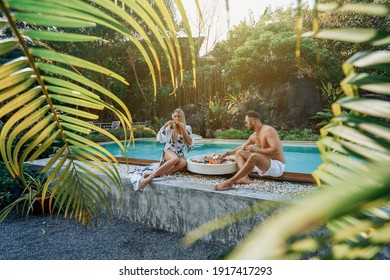 Pleased Couple Of A Man And A Woman In Swimsuit They Eat Tropical Food. Sweet Couple In Hotel On Their Honeymoon.