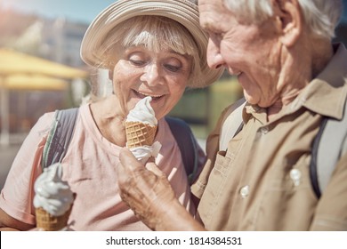 Pleased Cute Senior Lady In A Sunhat Eating Vanilla Ice Cream From Her Husband Hand