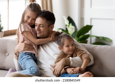 Pleased dad sit on couch with kids, after long separation missed his two little 7s daughters, closing his eyes, hugs them enjoying moment. Family bond and love, Happy Father Day celebration concept