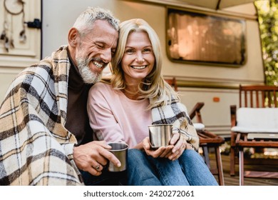 Pleased european mature couple spouses husband and wife sitting together on the van trailer motor home porch covered with blanket with mugs of coffee. - Powered by Shutterstock