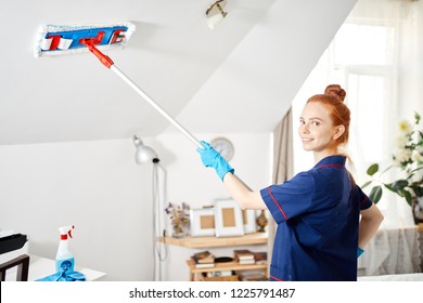 Pleased Happy Redhead Maid Woman Holding Mop Pile, Cleaning Ceiling At Vacant Hotel Room. House Cleaning Service Concept.