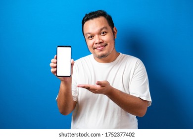 Pleased Happy Young Fat Asian Guy In White T-shirt Smiling To Camera While Holding Smartphone Pointing At Cellphone Screen