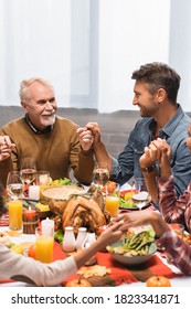 Pleased Multicultural Family Holding Hands During Dinner On Thanksgiving Holiday