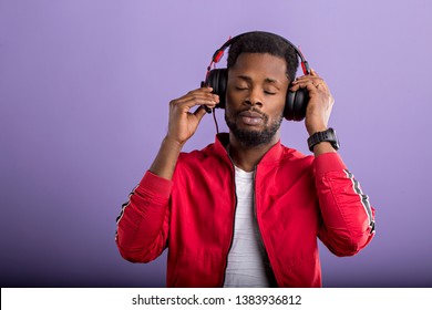 Pleased relaxed bearded stylish dark skinned man listening romantic song in modern black headphones, enjoying with closed eyes on violet background. Positive emotions, enjoyment, music. - Powered by Shutterstock