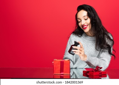 Pleased Woman Holding Bottle With Perfume Near Gift Box Isolated On Red