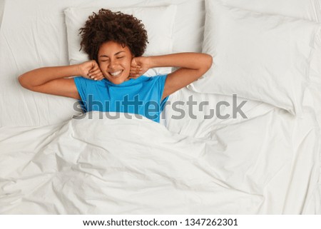 Pleased woman smiles happily, has sweet dreams, sleeps well in cozy bed, enjoys healthy good sleep or nap, expresses happiness, closes eyes. Pleasure concept. Starting new day in high spirit