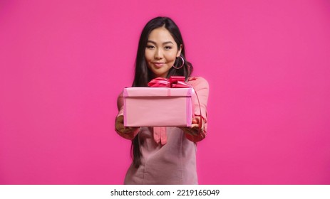 Pleased Young Asian Woman Holding Wrapped Present Isolated On Pink 