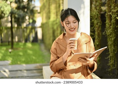 Pleased young Asian woman with take away coffee reading book outdoor on sunny day. - Powered by Shutterstock