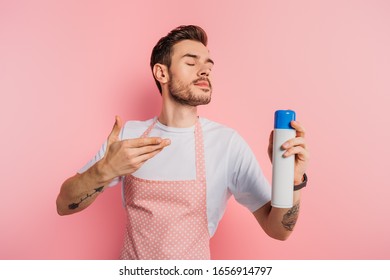 Pleased Young Man In Apron Enjoying Smell Of Air Freshener On Pink Background