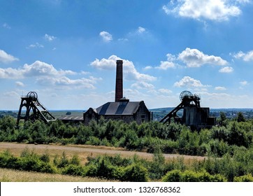 PLEASLEY, UK - MARCH 1, 2019: Red brick chimney, stone engine house, headstocks and winding gear under blue summer sky at Grade II listed Pleasley Colliery Mining Heritage Museum, Derbyshire, UK