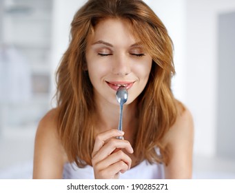 Pleasure From Eating / Portrait Of Young Smiling Woman With Spoon In Her Mouth 