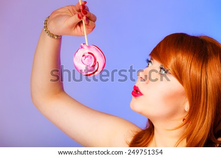Pleasure of eating sweets. Pretty young girl with lollipop in hands on purple and blue background. Studio shot.