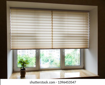Pleated blinds XL, beige color, with 50mm fold closeup in the window opening in the interior. Home blinds - modern bottom up privacy shades half raised on apartment windows.           