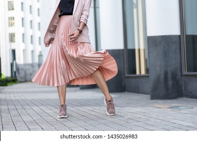 Pleated skirt coral color and sneakers. The girl is very dynamic posing on the street, the skirt is developing.