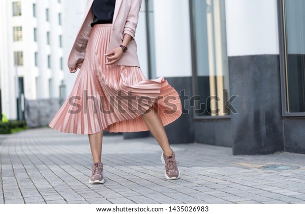 Pleated skirt coral\
color and sneakers. The girl is very dynamic posing on the street,\
the skirt is\
developing.