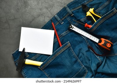 Pliers, hammer, screwdriver and tape measure in the pocket of jeans and a blank card for a you text on a blue background. Give a present to dad. Happy fathers day concept. Labor day. copy space 