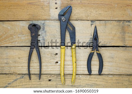 Pliers, needle nose, and nail remover spread out of rough wooden background. 