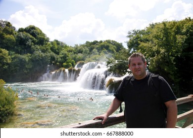 PLITVICE, CROATIA - 10. JUNE 2017 A young man is posing for a photo on the bridge and there is a waterfall in the background.