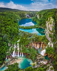 Plitvice, Croatia - Panoramic View Of The Beautiful Waterfalls Of Plitvice Lakes In Plitvice National Park On A Bright Summer Day With Blue Sky And Clouds And Green Foliage And Turquoise Water