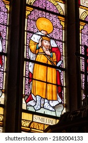 PLOUMILLIAU, FRANCE - Aug 9, 2018: Stained Glass Window Depicting Saint Milliau Of Cornwall Holding His Beheaded Or Decapitated Head Inside The Church