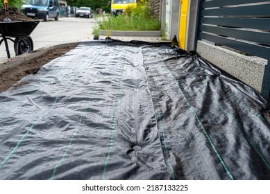 The plowed garden in front of the fence in the house, covered with black agrofiber, visible black plastic pin.