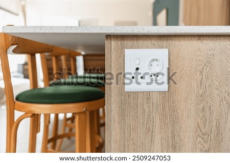 Plug point mounted on the side of a kitchen island, wood look cabinets, white stone surface, green bar chairs